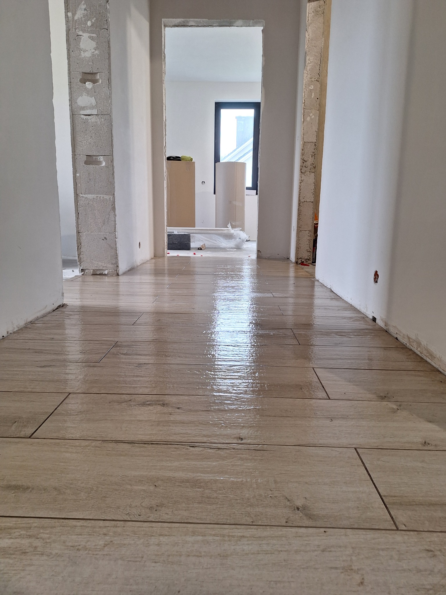 Świeżo ułożone, błyszczące panele podłogowe imitujące drewno w korytarzu, widoczne surowe ściany i niedokończone ościeżnice.