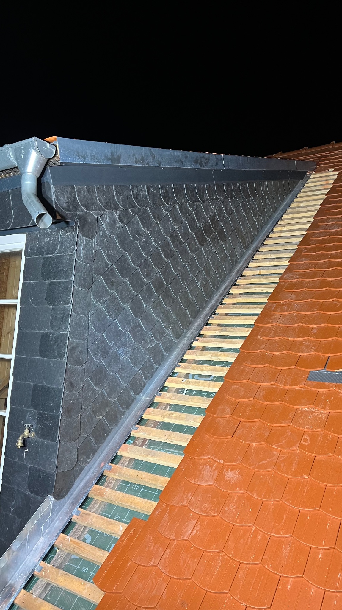 Fragment dachu w trakcie układania: część pokryta łupkiem, część z czerwoną dachówką, widoczne łaty i membrana dachowa, orynnowanie.