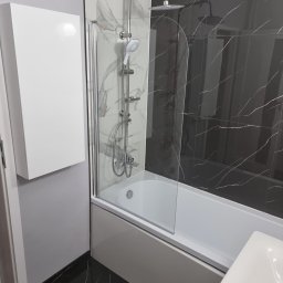 Mateusz Wardyński - Nowoczesna łazienka z czarno-białymi marmurkowymi płytkami, białą wanną z parawanem i szafką. Czarne płytki podłogowe z białymi żyłkami.