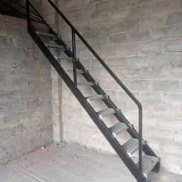 DAMET Damian Micuła - Metalowe schody drabinkowe z poręczą, prowadzące w górę, ustawione przy ścianie z szarej cegły