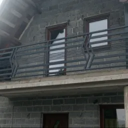 Nowoczesna, pozioma balustrada balkonowa z metalu w kolorze grafitowym, z geometrycznym wzorem, zamontowana na betonowym balkonie domu z szarej cegły.