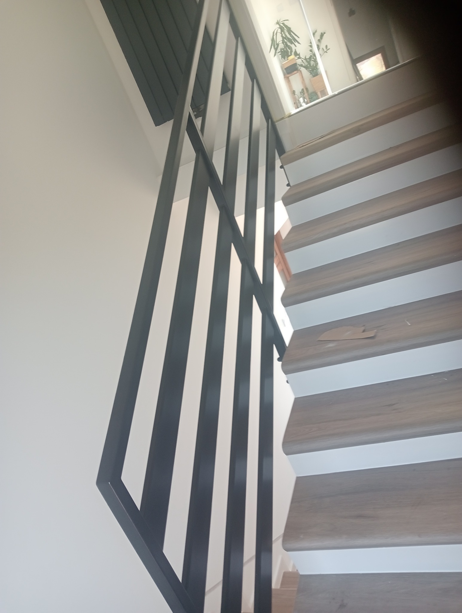 Nowoczesna, czarna balustrada schodowa z pionowych profili, drewnopodobne schody z białymi podstopnicami, widok z dołu.