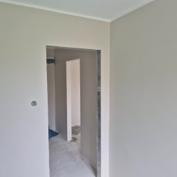 Bogusław Paszek - Wnętrze po malowaniu na jasny odcień szarości, widoczne gładkie ściany i ościeżnica drzwiowa. Na ścianie widoczna puszka elektryczna.