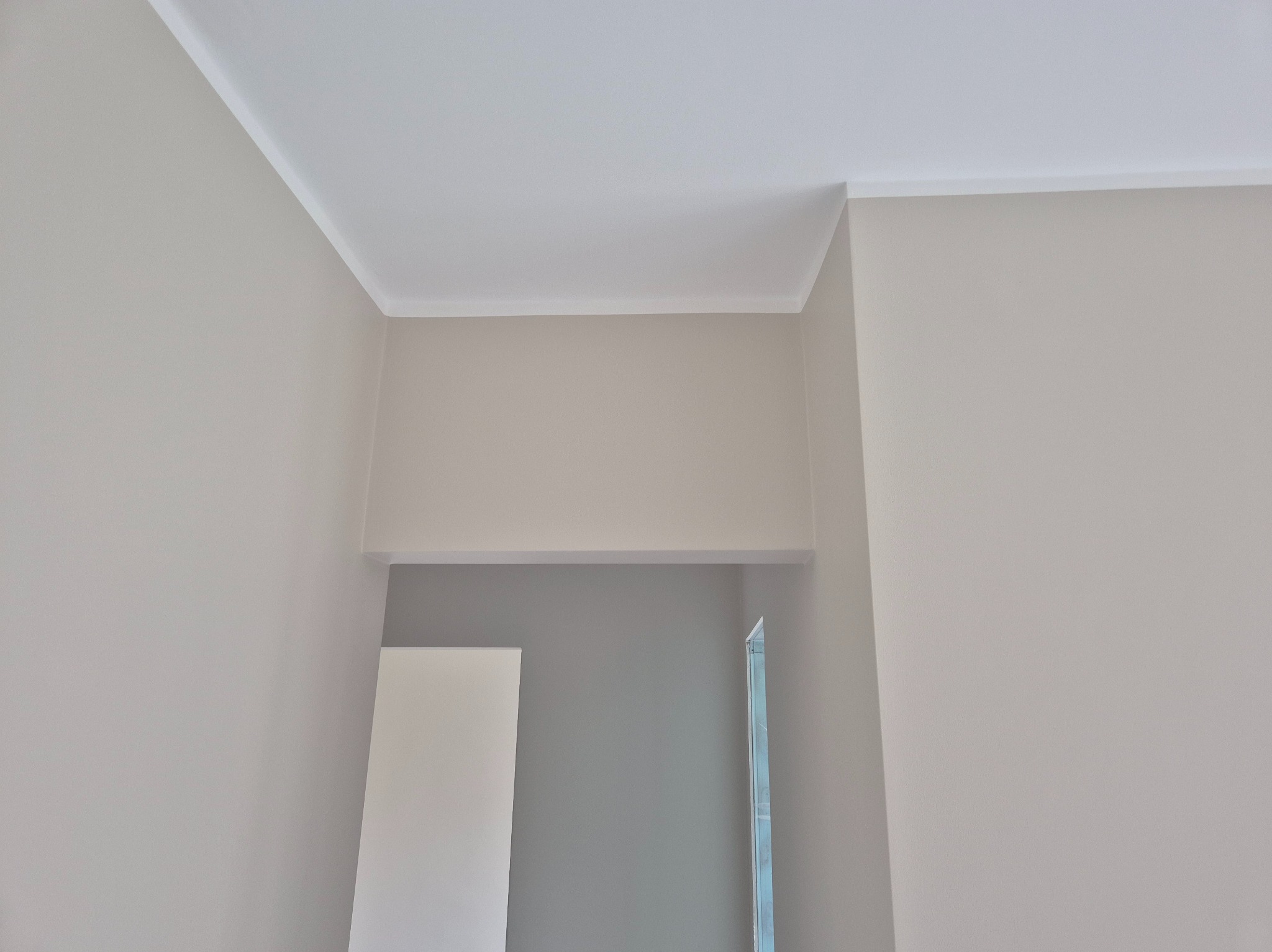 Jasne ściany po malowaniu z dekoracyjną listwą przysufitową, widoczne fragmenty drzwi i ościeżnicy. Minimalizm i czystość w wykończeniu wnętrza.