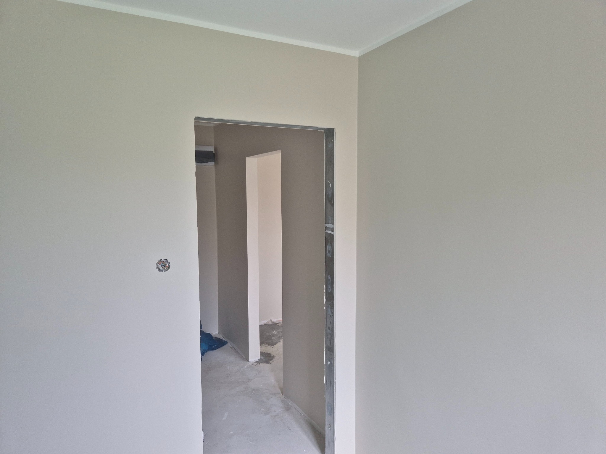 Wnętrze po malowaniu na jasny odcień szarości, widoczne gładkie ściany i ościeżnica drzwiowa. Na ścianie widoczna puszka elektryczna.