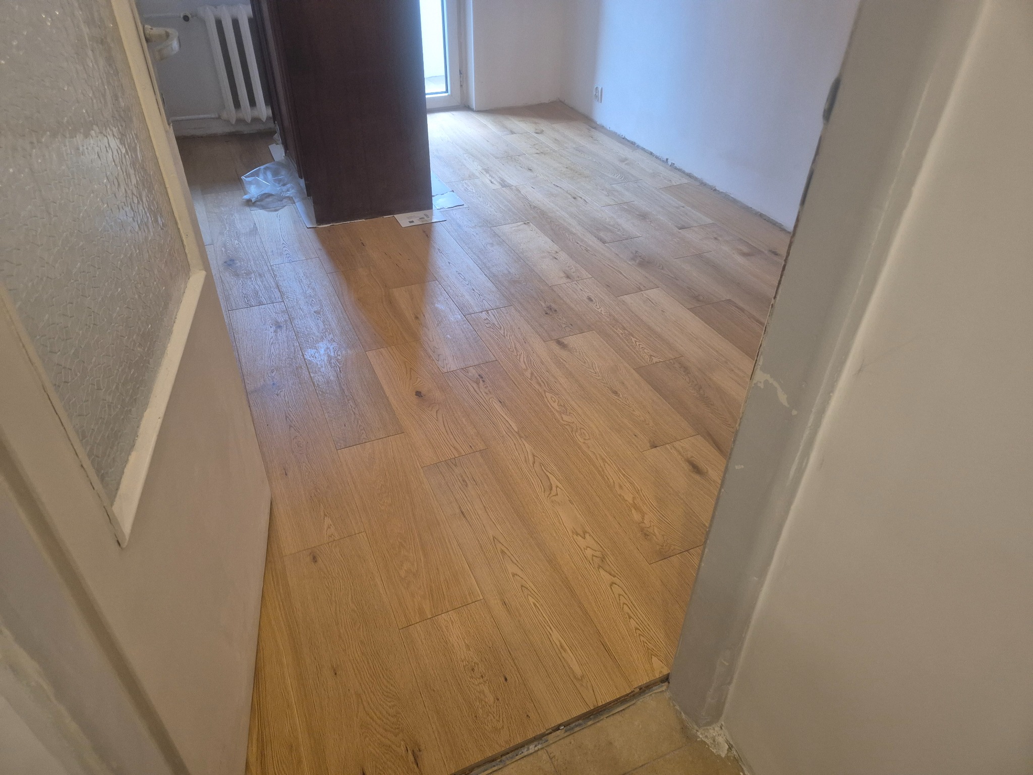 Ułożone panele podłogowe w jasnym odcieniu drewna, widoczne z perspektywy wejścia do pokoju, z fragmentem drzwi po lewej i prawej stronie kadru.