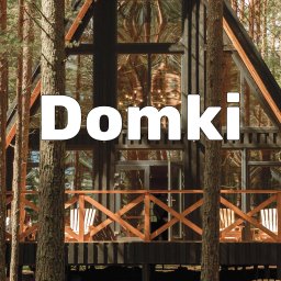 Gardea - Nowoczesny dom w kształcie litery A z dużymi oknami, drewnianym tarasem i balustradą, wkomponowany w leśny krajobraz z widocznymi pniami drzew.