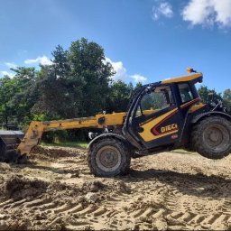 Firma Handlowo Usługowa - Żółto-czarna ładowarka teleskopowa Dieci z pełną łyżką unosi się na nierównym, piaszczystym terenie budowy, z widocznymi śladami opon i lasem w tle pod błękitnym niebem.