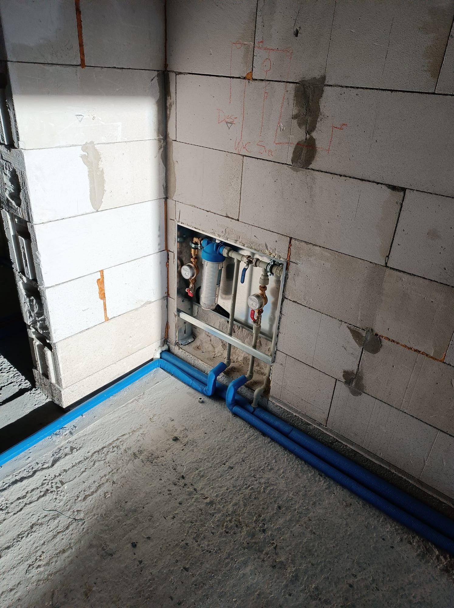 Fragment instalacji hydraulicznej z filtrem i manometrami, widoczne niebieskie rury w ścianie z betonu komórkowego, Miedźna, w trakcie montażu.