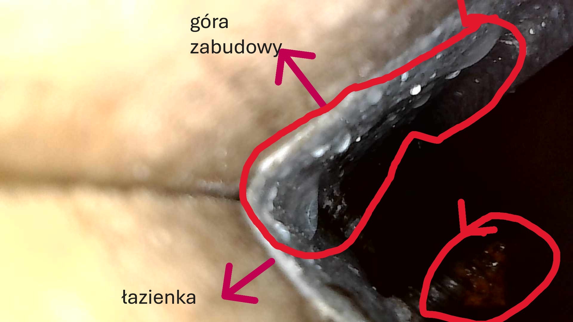 Fragment zabudowy w łazience, widoczne elementy konstrukcyjne i wykończeniowe. Narożnik z widocznymi śladami wilgoci lub uszczelnienia. Niejasne oświetlenie.