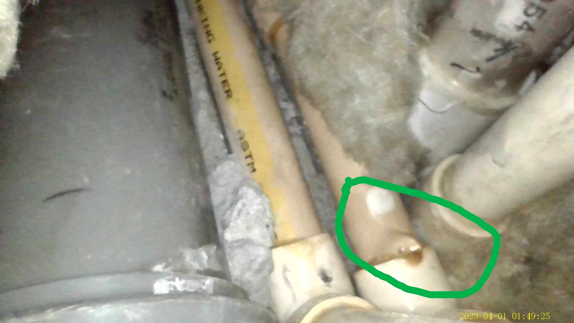 Wyciekająca rura z widocznym uszkodzeniem i śladami naprawy. Żółta rura z napisem 'DRINKING WATER'. Widoczne elementy instalacji w izolacji.