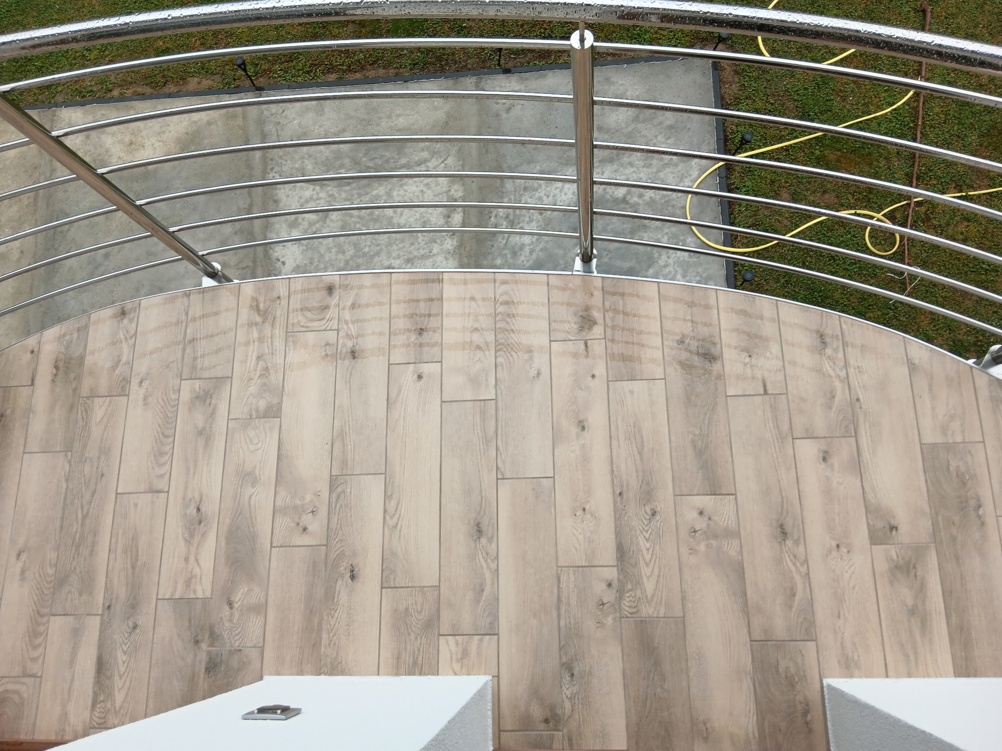 Jasne panele ułożone na balkonie w Osieku Jasielskim, widok z góry. Metalowa balustrada balkonowa. Na zewnątrz trawa i beton.