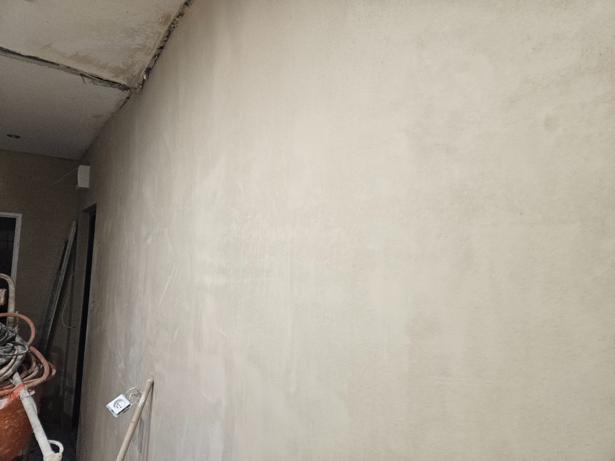 Świeżo otynkowana ściana wewnętrzna w trakcie remontu, widoczne narzędzia i gniazdko elektryczne bez osprzętu.