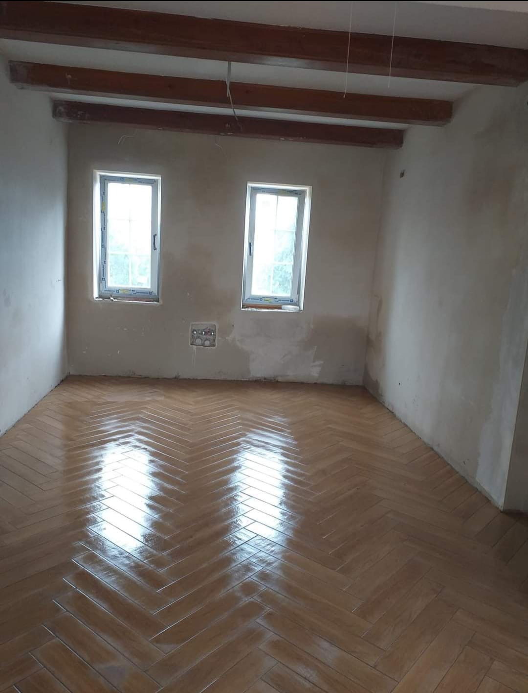 Pokój z nowo ułożonym parkietem w jodełkę, surowe ściany czekają na malowanie, widoczne drewniane belki stropowe.