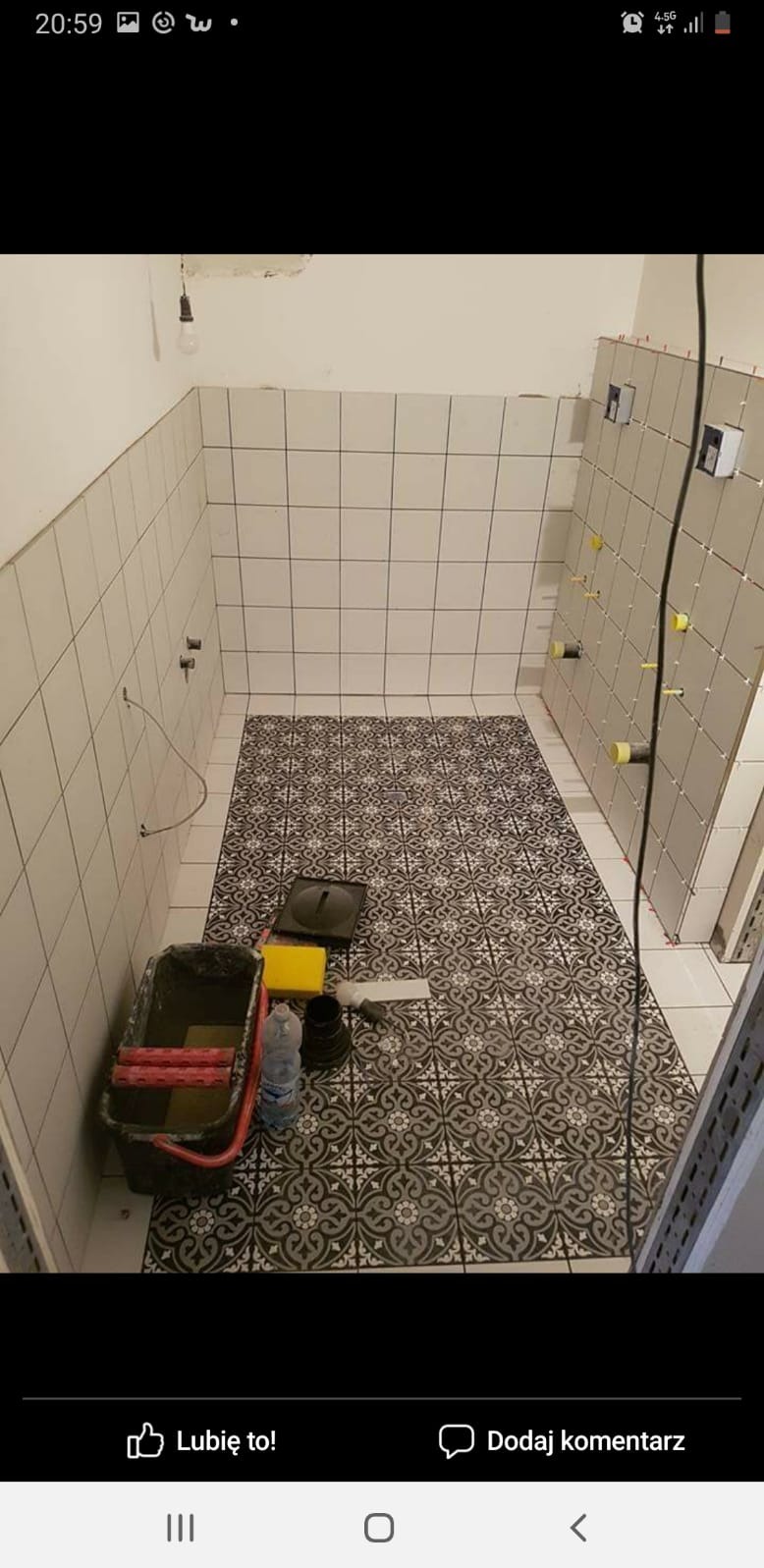 Wnętrze łazienki w trakcie remontu: ułożona wzorzysta podłoga, częściowo wykafelkowane ściany z widocznymi uchwytami do armatury, obok wiadro z narzędziami do malowania.