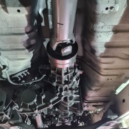 A&S Auto Centrum Serwis 4x4 Jeep Toyota Nissan Suzuki Konserwacja podwozi ram - Widok podwozia samochodu z widocznym wałem napędowym, skrzynią biegów i elementami zawieszenia po niedawnym zabezpieczeniu antykorozyjnym, świecące elementy po malowaniu, widoczne ślady...