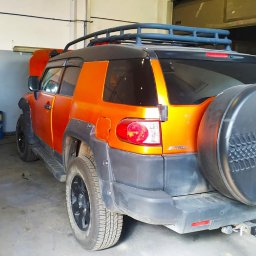 A&S Auto Centrum Serwis 4x4 Jeep Toyota Nissan Suzuki Konserwacja podwozi ram - Pomarańczowy Toyota FJ Cruiser z otwartą maską w warsztacie, widoczny bagażnik dachowy i koło zapasowe z tyłu.