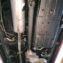 A&S Auto Centrum Serwis 4x4 Jeep Toyota Nissan Suzuki Konserwacja podwozi ram - Podwozie Toyoty po konserwacji antykorozyjnej, widoczny tłumik i elementy ramy pokryte czarną powłoką ochronną, auto podniesione na podnośniku.