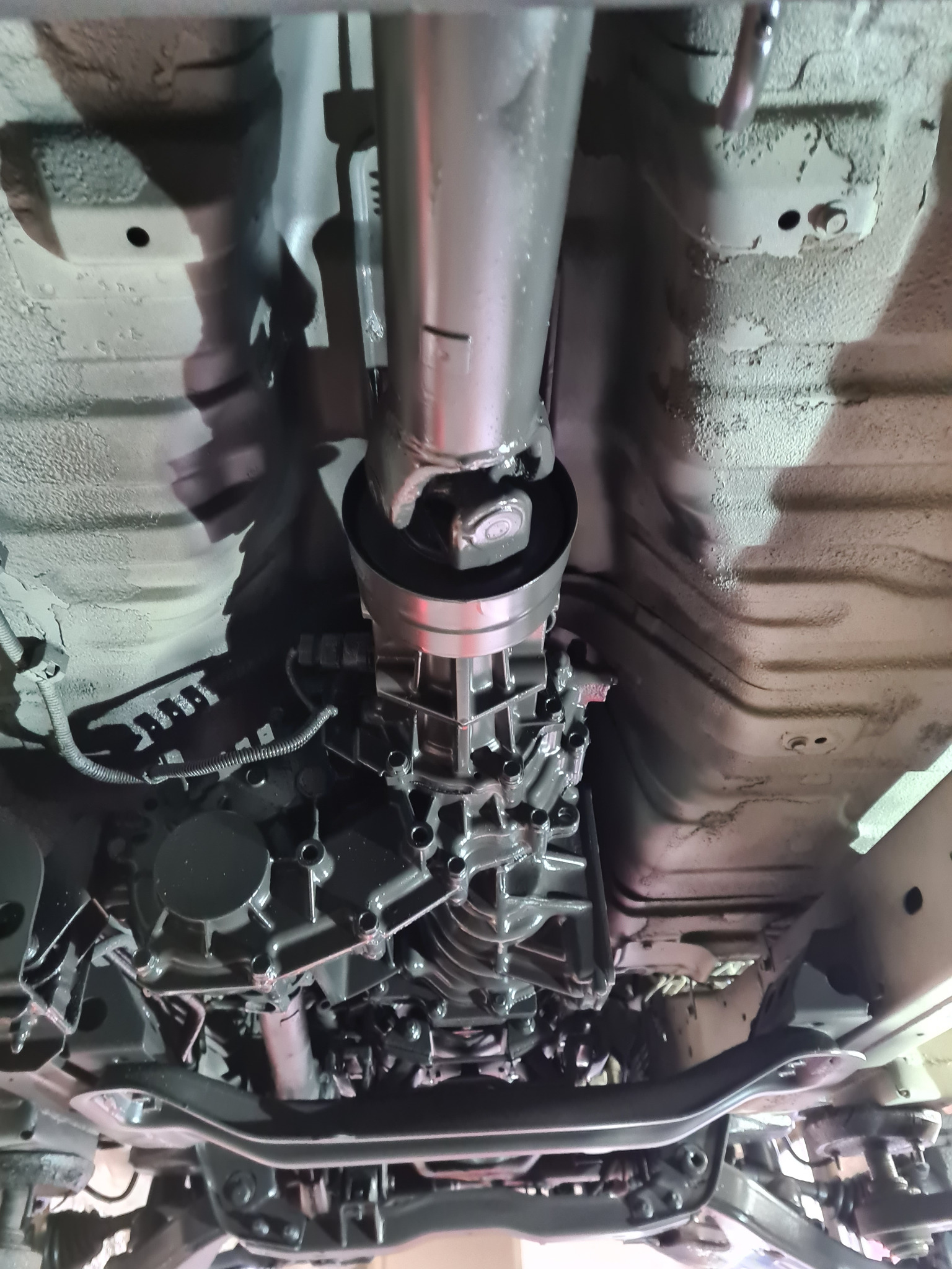 Widok podwozia samochodu z widocznym wałem napędowym, skrzynią biegów i elementami zawieszenia po niedawnym zabezpieczeniu antykorozyjnym, świecące elementy po malowaniu, widoczne ślady...