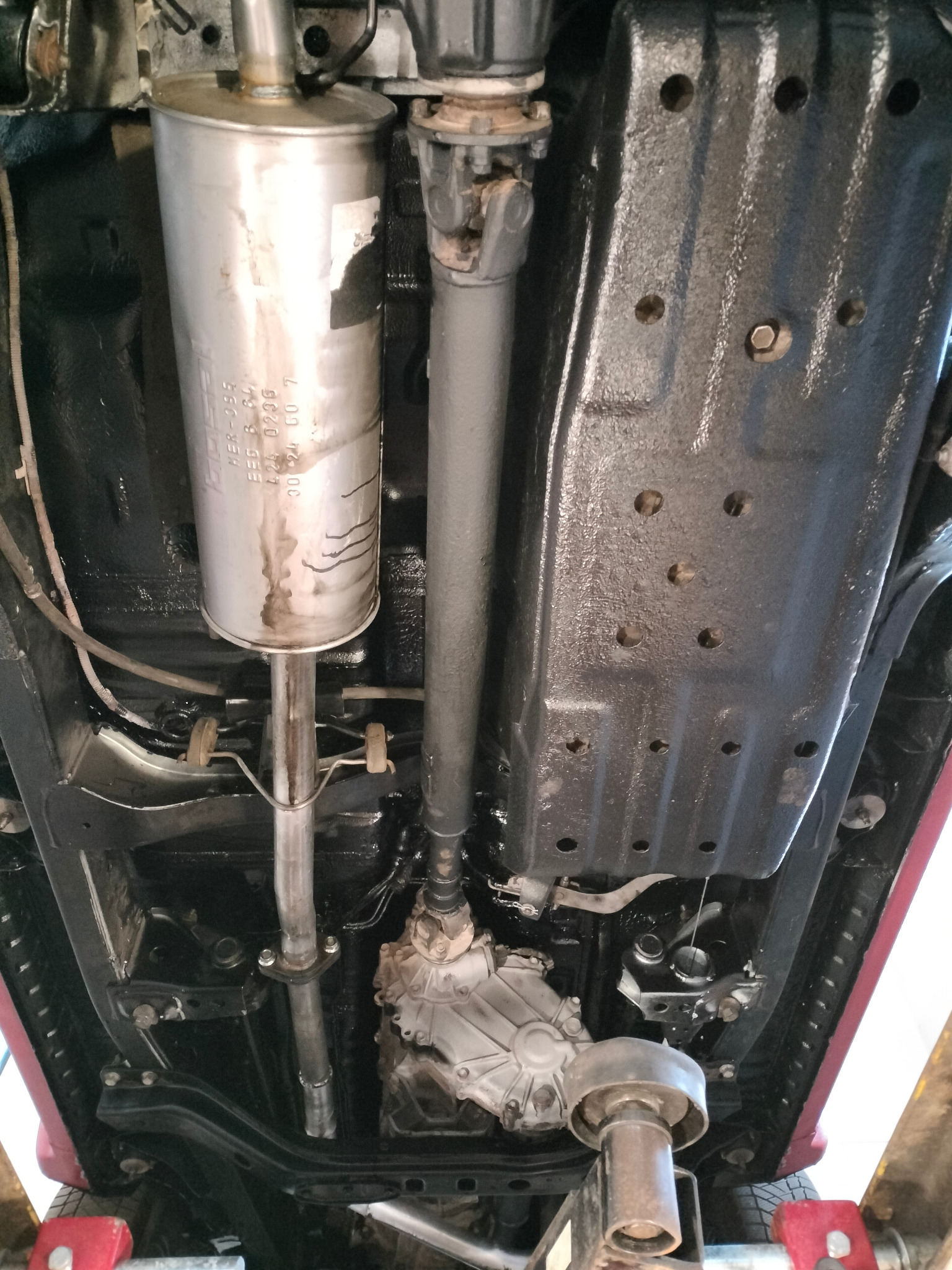 Podwozie Toyoty po konserwacji antykorozyjnej, widoczny tłumik i elementy ramy pokryte czarną powłoką ochronną, auto podniesione na podnośniku.