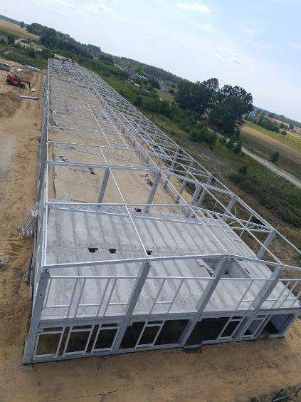 Szkielet konstrukcji hali stalowej z betonową wylewką podłoża, widok z góry, teren budowy z koparką w tle.