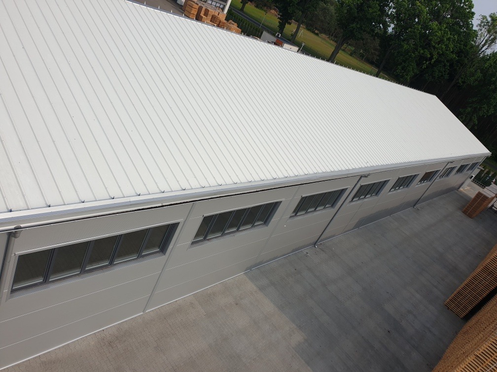 Gotowa hala przemysłowa z szarej płyty warstwowej z rzędem okien, widok z góry na dach i elewację.