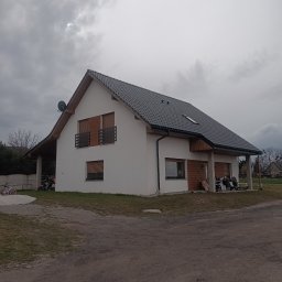 Darfiko - Nowoczesny, parterowy dom z szarym dachem i drewnianymi elementami wykończeniowymi, widok z zewnątrz w pochmurny dzień.