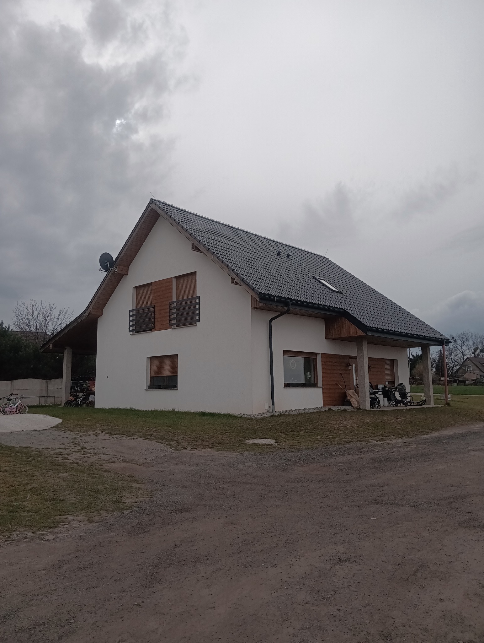 Nowoczesny, parterowy dom z szarym dachem i drewnianymi elementami wykończeniowymi, widok z zewnątrz w pochmurny dzień.