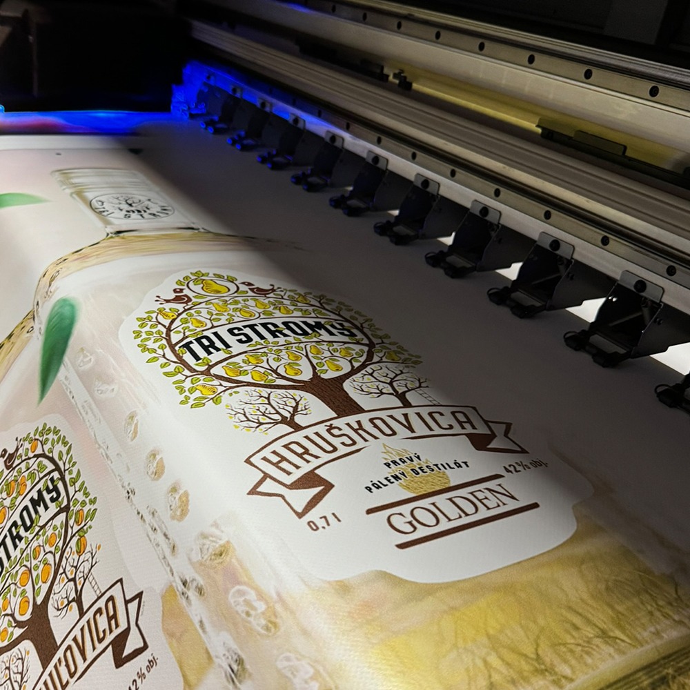Drukarka wielkoformatowa w trakcie drukowania etykiet na butelki z motywem drzewa owocowego i napisem 'TRI STROMS HRUŠKOVICA'