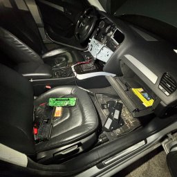 BAI-AUTO Oleksandr Baidiuk - Wnętrze samochodu z rozmontowanym radiem i elementami elektrycznymi na skórzanym siedzeniu, wnętrze w trakcie naprawy, widoczne przewody i elementy elektroniki.