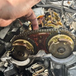 BAI-AUTO Oleksandr Baidiuk - Silnik samochodowy w trakcie naprawy: widoczny łańcuch rozrządu, koła zębate i ręka mechanika wskazująca na element. Detaliczne ujęcie wnętrza silnika.