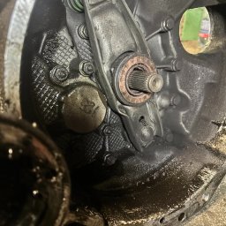 BAI-AUTO Oleksandr Baidiuk - Detal skrzyni biegów z widocznym łożyskiem oporowym i dźwignią sprzęgła, pokrytych olejem. Widoczne śruby i fragment otworu w obudowie.