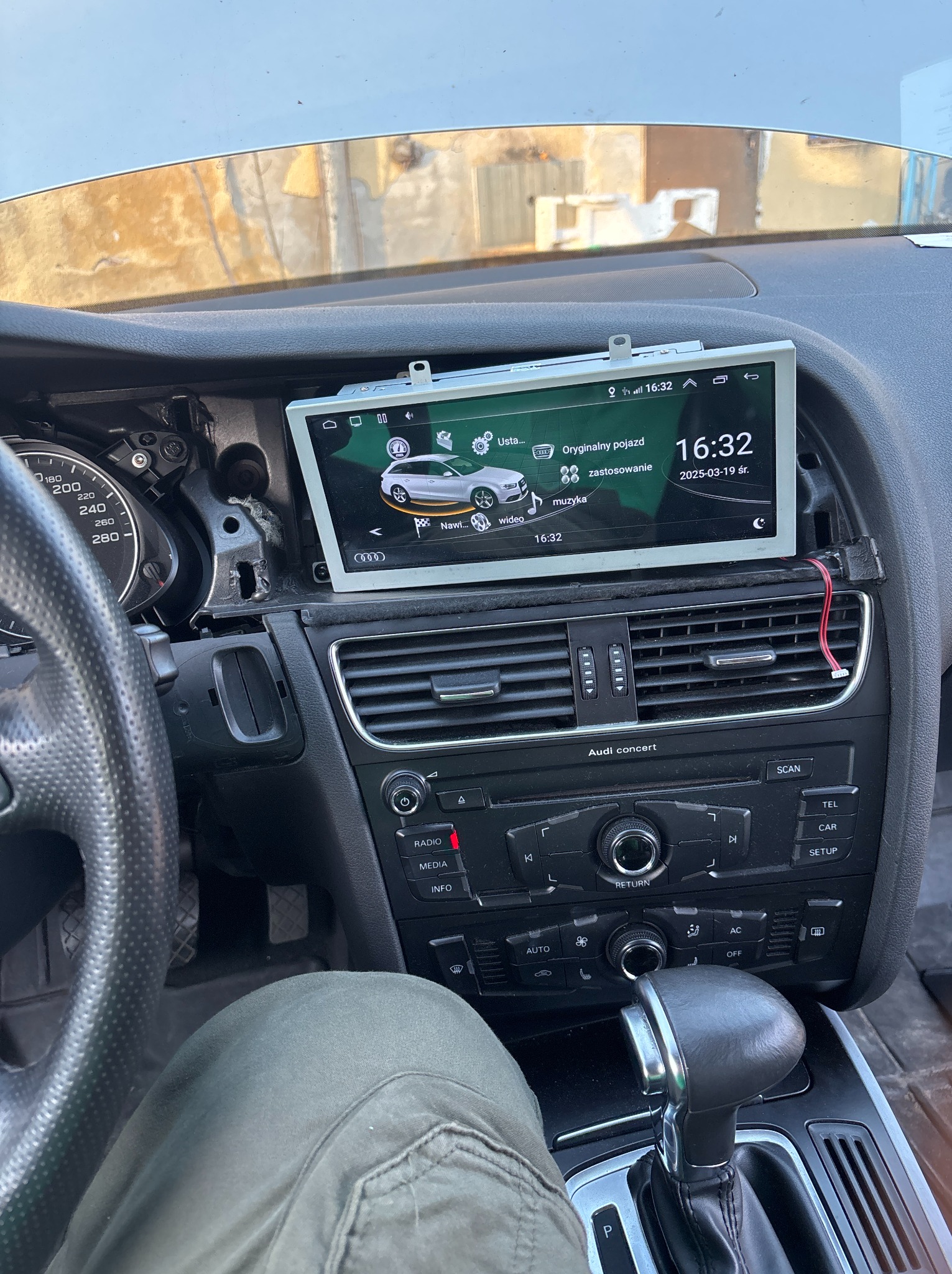 Montaż nowego radia samochodowego w desce rozdzielczej Audi A5. Widoczne elementy wnętrza pojazdu i wyświetlacz z systemem nawigacji. Prace w toku.