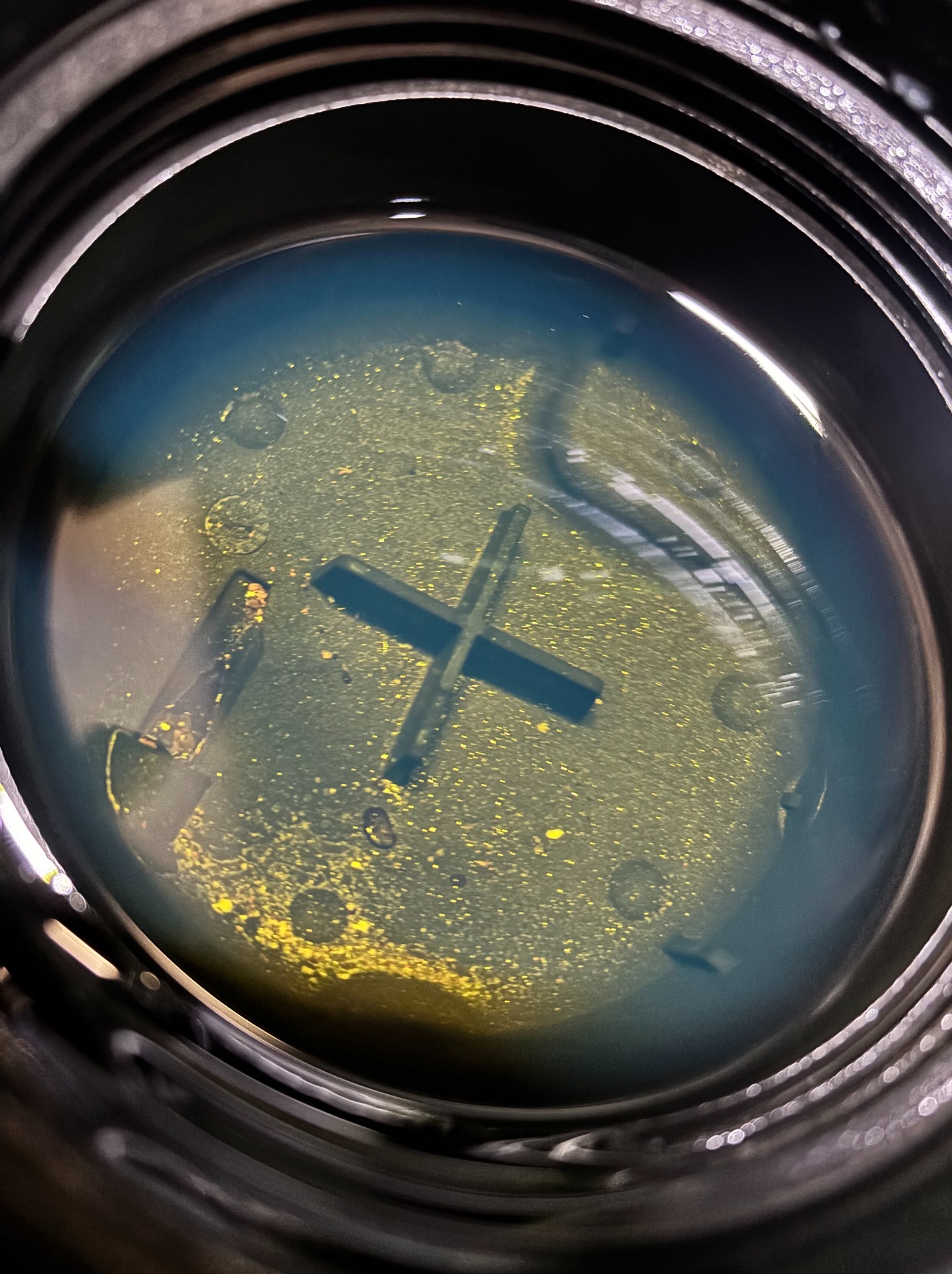 Zbliżenie na wlew zbiornika płynu chłodniczego z widocznym zanieczyszczeniem. Widoczny osad i zmiana koloru płynu. Plastikowy korek wlewu.