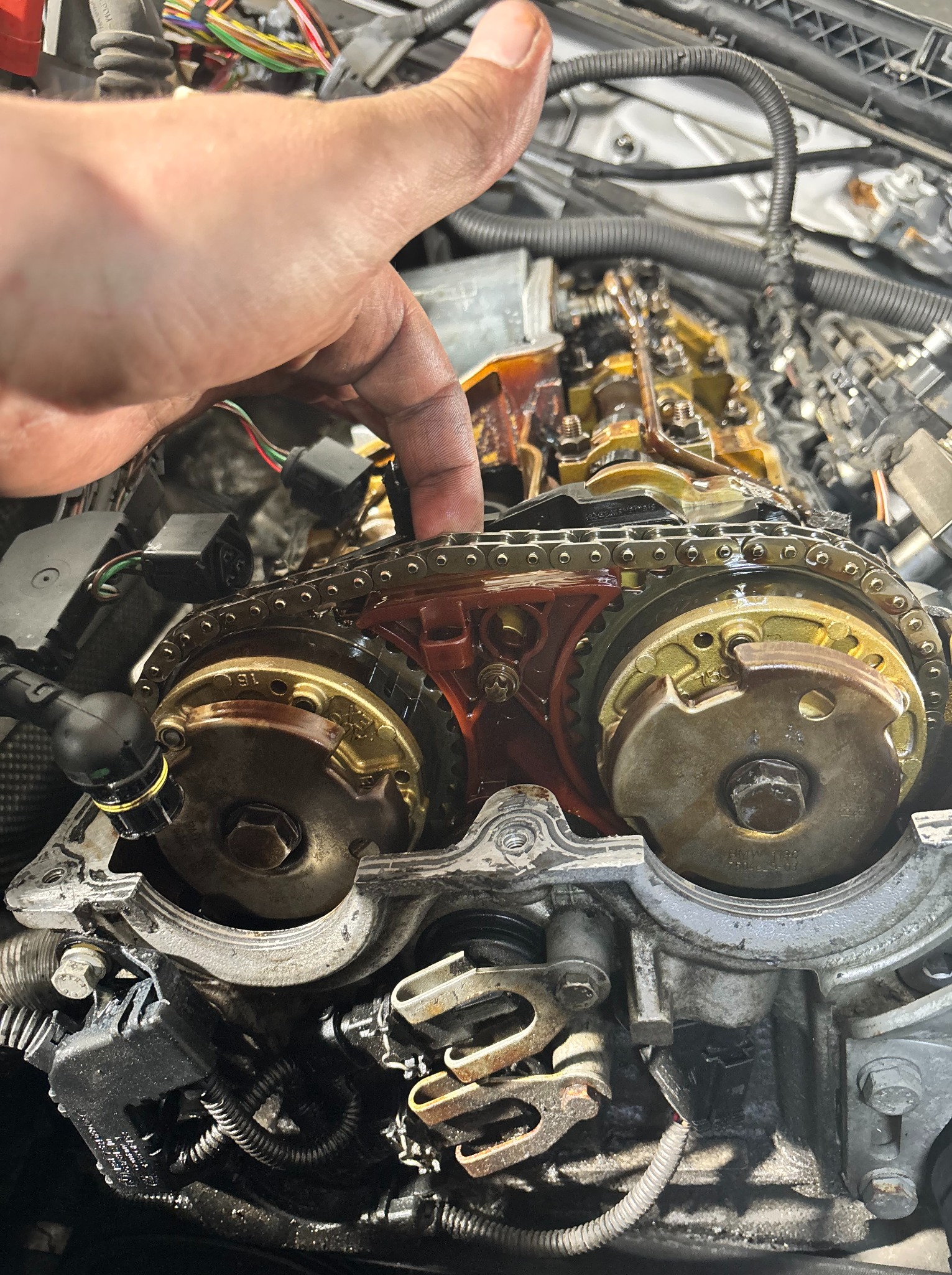 Silnik samochodowy w trakcie naprawy: widoczny łańcuch rozrządu, koła zębate i ręka mechanika wskazująca na element. Detaliczne ujęcie wnętrza silnika.