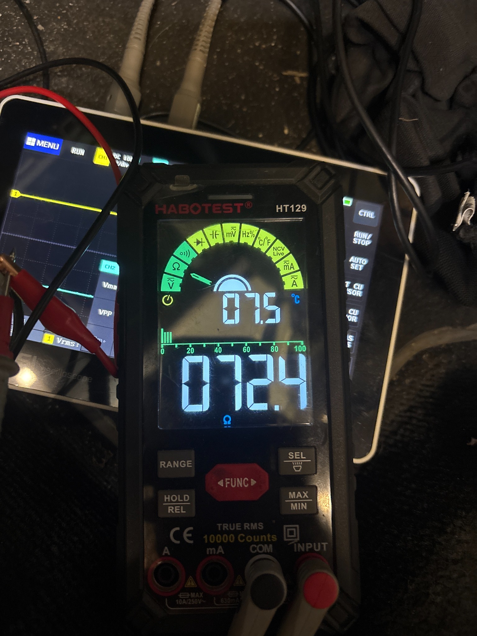 Pomiar elektryczny: Multimetr Habotest HT129 pokazuje wartości 07.5°C i 072.4 Ω. Obok oscyloskop z widocznym wykresem. Kable pomiarowe podłączone.