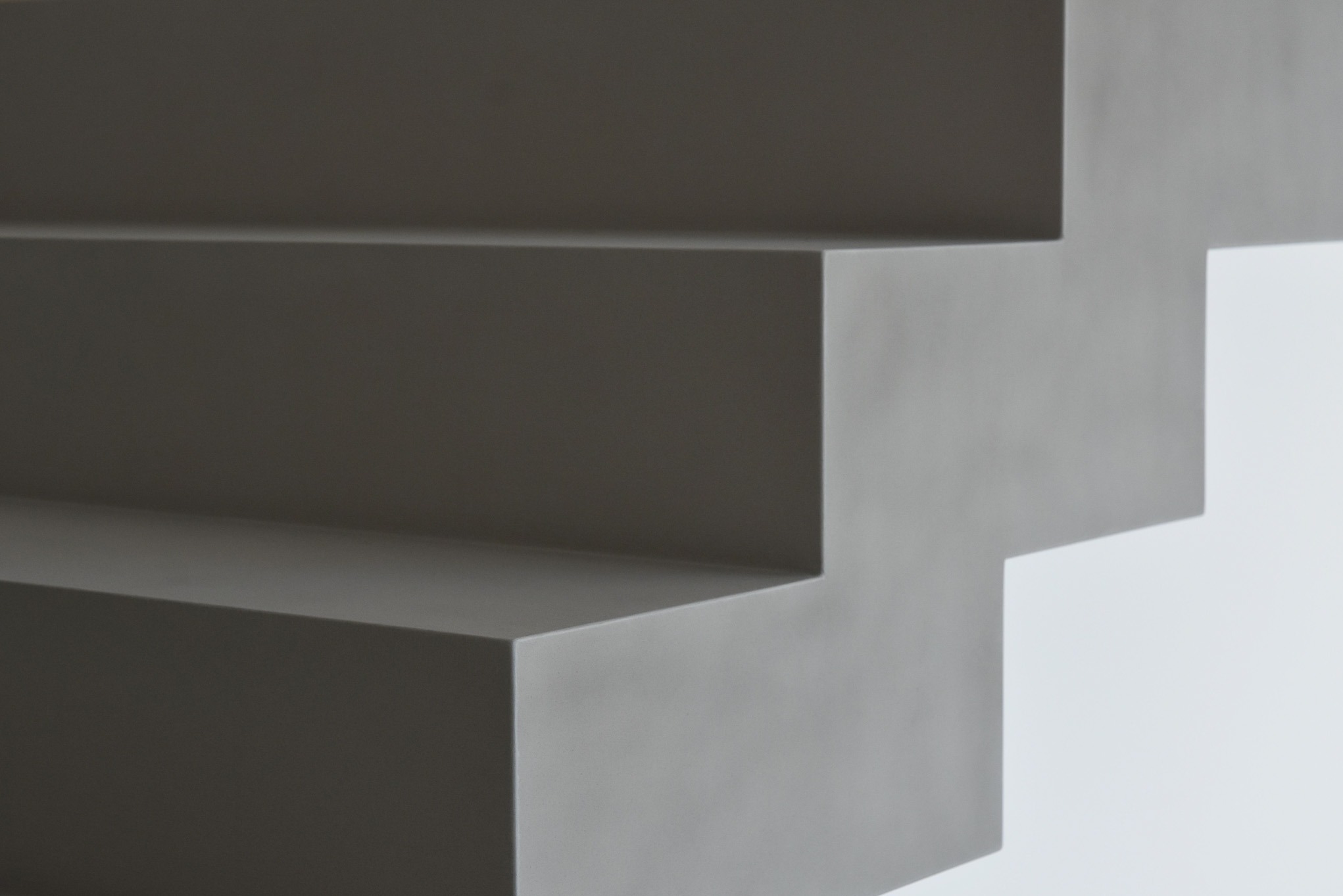 Minimalistyczne schody w odcieniach szarości, wykończone gładką powierzchnią, z widocznymi krawędziami i subtelnym światłocieniem.