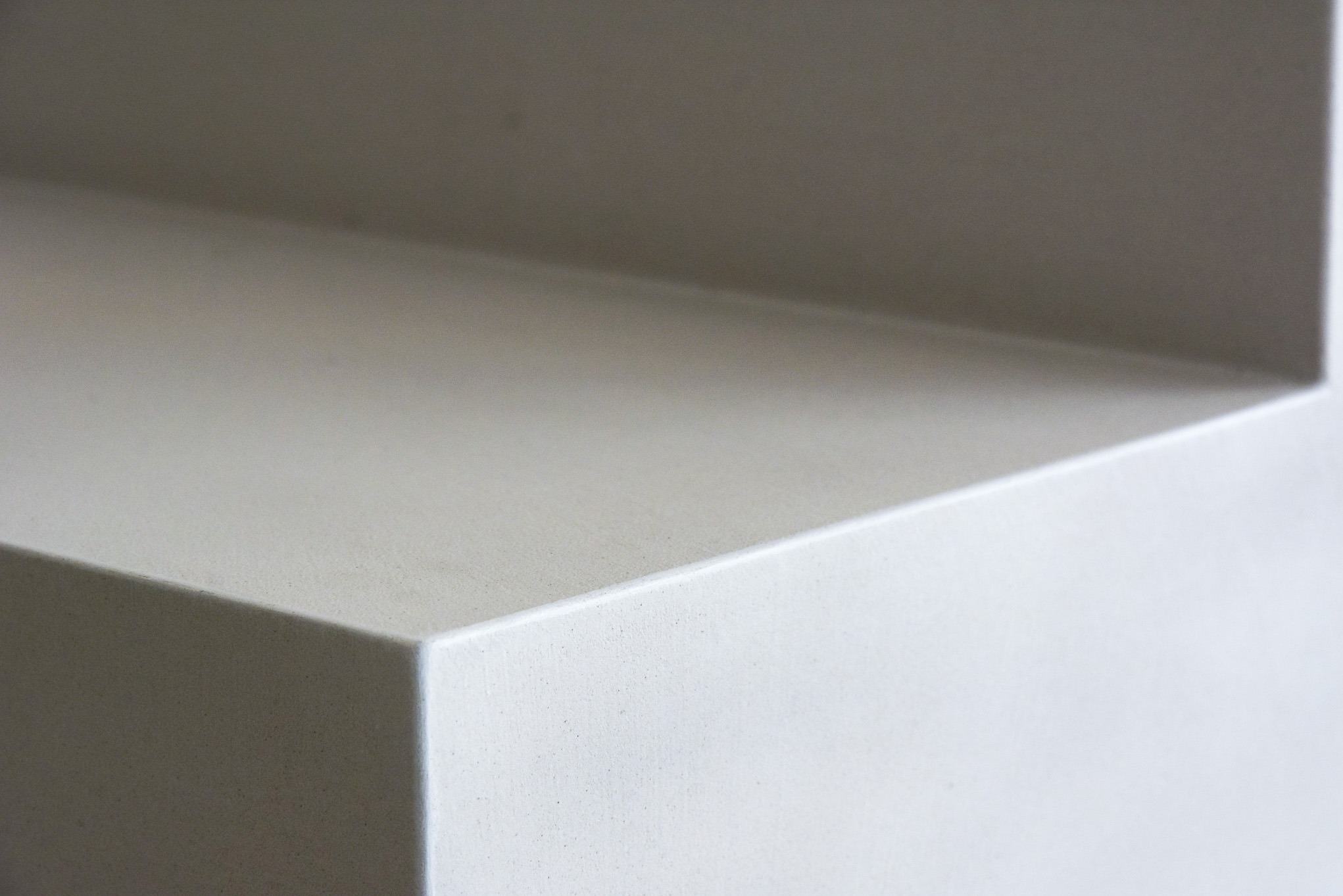 Minimalistyczne ujęcie narożnika ściany wykończonej jasnoszarą, gładką powierzchnią, eksponujące fakturę i precyzję wykonania.