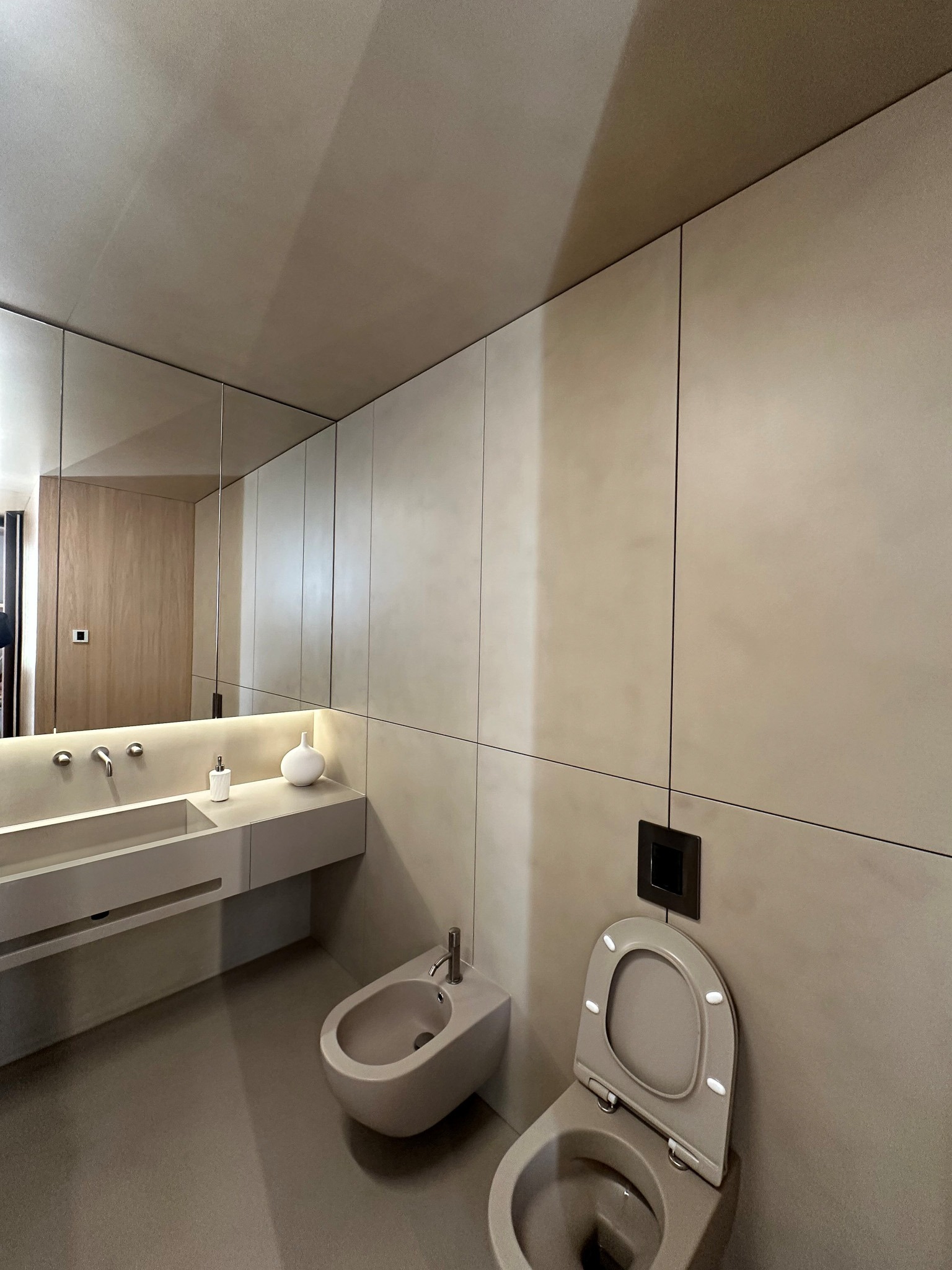 Minimalistyczna łazienka w odcieniach beżu z toaletą, bidetem i umywalką z lustrem, wykończona panelami ściennymi z delikatną fakturą.