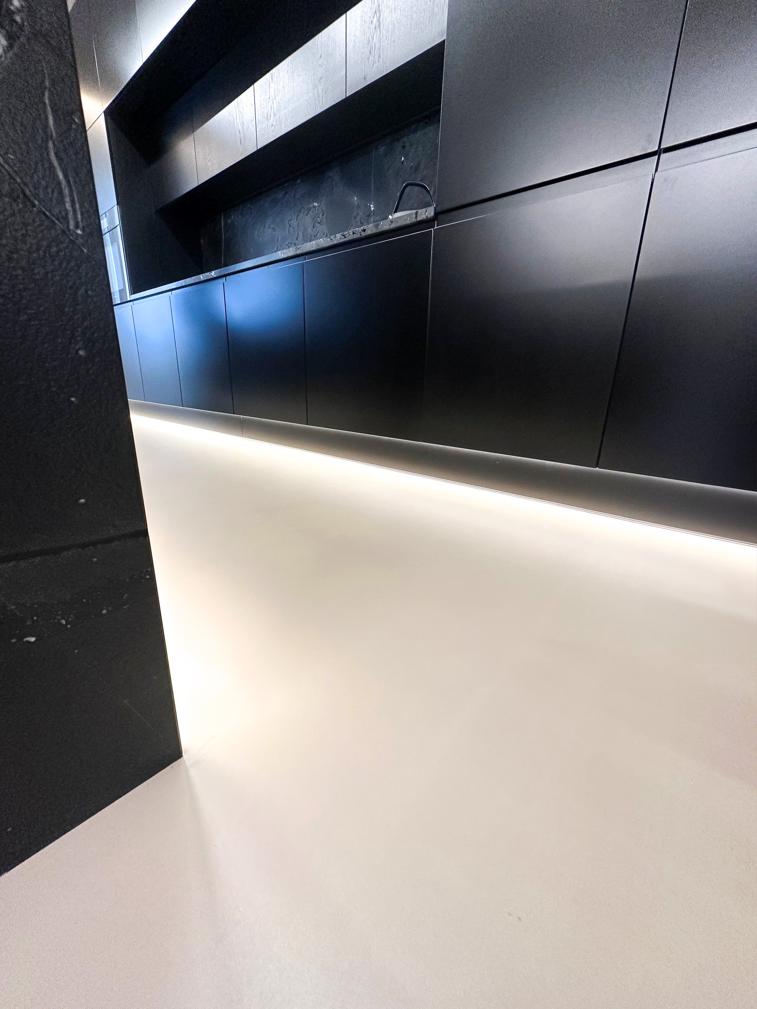 Nowoczesna kuchnia z czarnymi szafkami i jasną, gładką posadzką z oświetleniem LED pod szafkami, widok z dołu podkreślający minimalistyczny design.