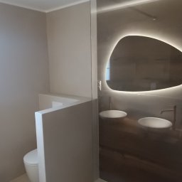 Mg Bud - Nowoczesna łazienka w beżach z podświetlanym lustrem o nieregularnym kształcie, kabiną prysznicową ze szkła i zabudowaną toaletą. Minimalistyczny design.