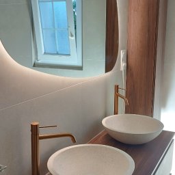 Mg Bud - Nowoczesna łazienka z dwoma umywalkami nablatowymi, złotymi bateriami i podświetlanym lustrem o nieregularnym kształcie. Widoczne okno z otwartym skrzydłem.