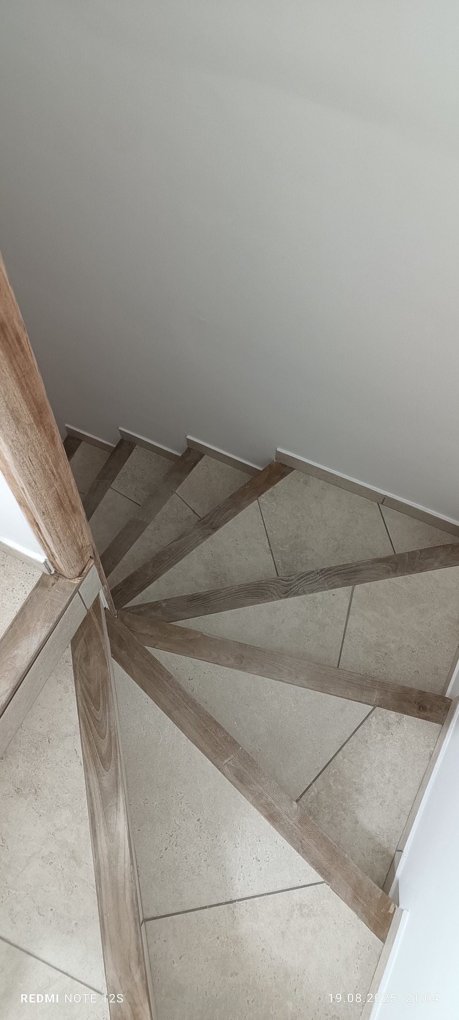 Spiralne schody z drewnianymi stopniami i beżowymi płytkami, widok z góry. Minimalistyczny design, jasne wnętrze, ukończony remont.