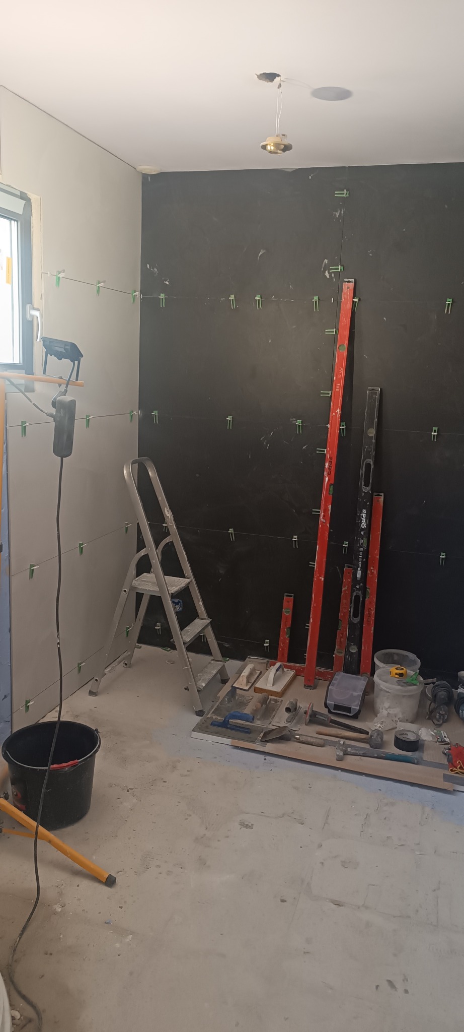 Przygotowanie do układania płytek w Poznaniu. Widoczne narzędzia glazurnicze, drabina i poziomice. Ściany częściowo pokryte płytkami, z zachowaniem odstępów.