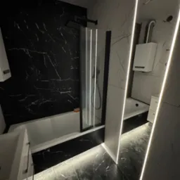 Nowoczesna łazienka z czarno-białymi płytkami imitującymi marmur, podświetleniem LED i kabiną prysznicową. Minimalistyczny design z akcentem na elegancję.