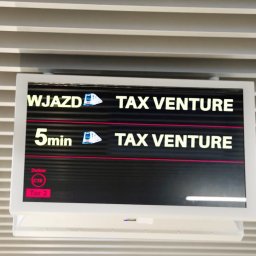 MATEUSZ RUBACH - Ekran informacyjny z napisem 'Wjazd' oraz '5min' i logotypem 'TAX Venture' na tle sufitu z żaluzjami i czerwonym czujnikiem pożarowym.