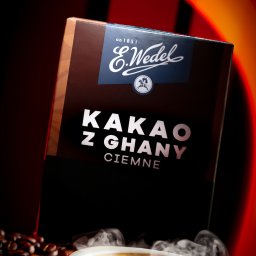 MATEUSZ RUBACH - Pudełko kakao E.Wedel z Ghany Ciemne, otoczone ziarnami kawy i parującą filiżanką latte art na czerwonym tle.