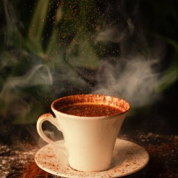 MATEUSZ RUBACH - Aromatyczna filiżanka kawy z unoszącym się pyłem kakaowym, otoczona ziarnami kawy i subtelną parą na ciemnym tle.