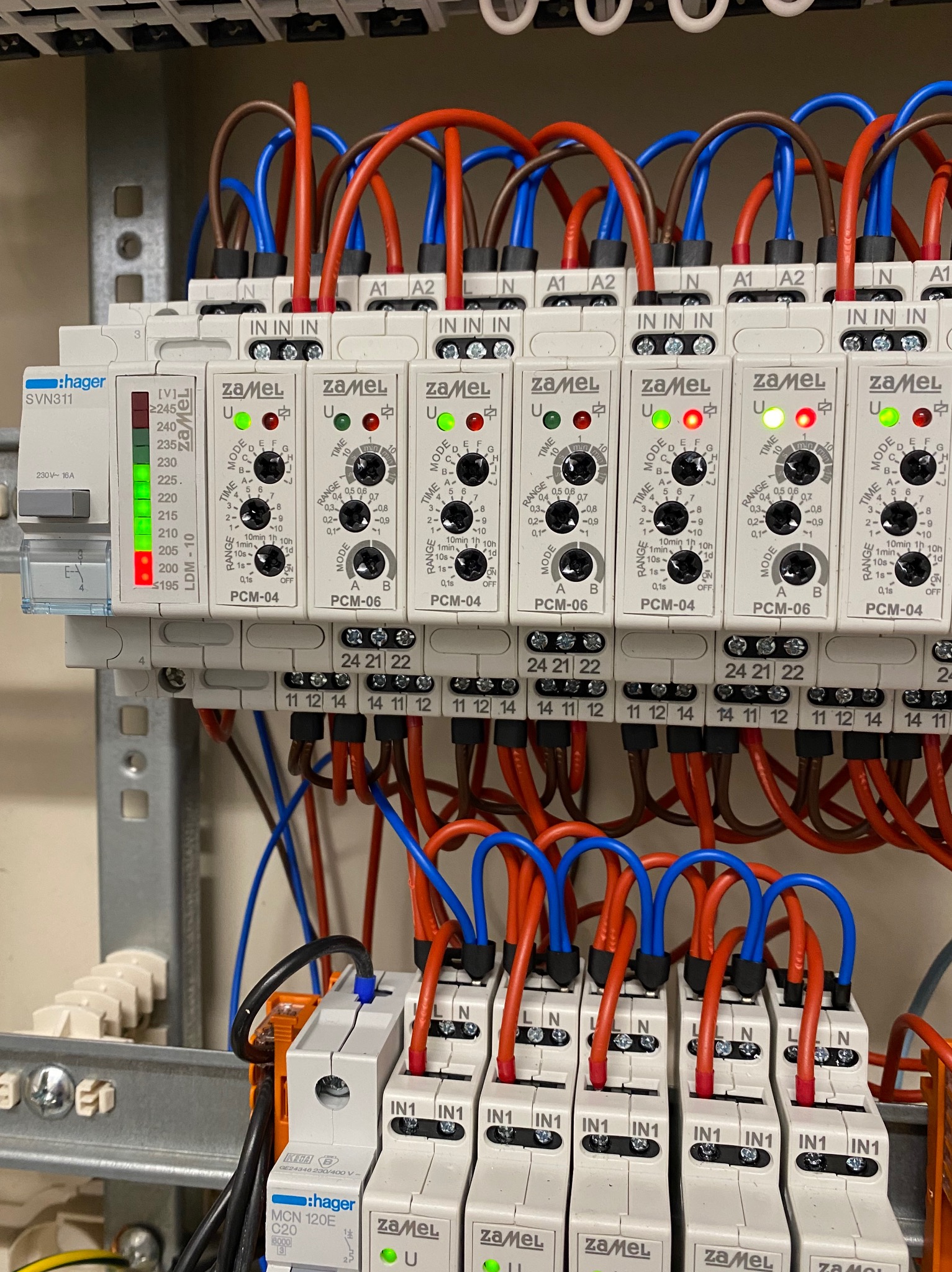 Rozdzielnia elektryczna z zamontowanymi przekaźnikami czasowymi Zamel PCM-04 i PCM-06, z podłączonymi przewodami w kolorach niebieskim, czerwonym i brązowym.