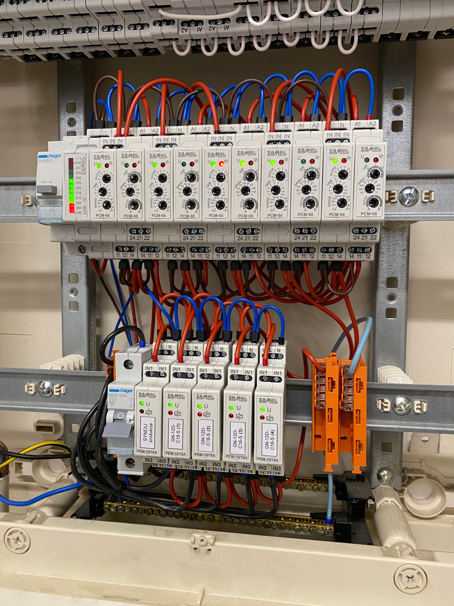 Rozdzielnia elektryczna z modułami Zamel PCM-04 i PCM-06, zabezpieczeniami Hager, oraz okablowaniem w kolorach niebieskim i czerwonym. Widoczne diody sygnalizacyjne.